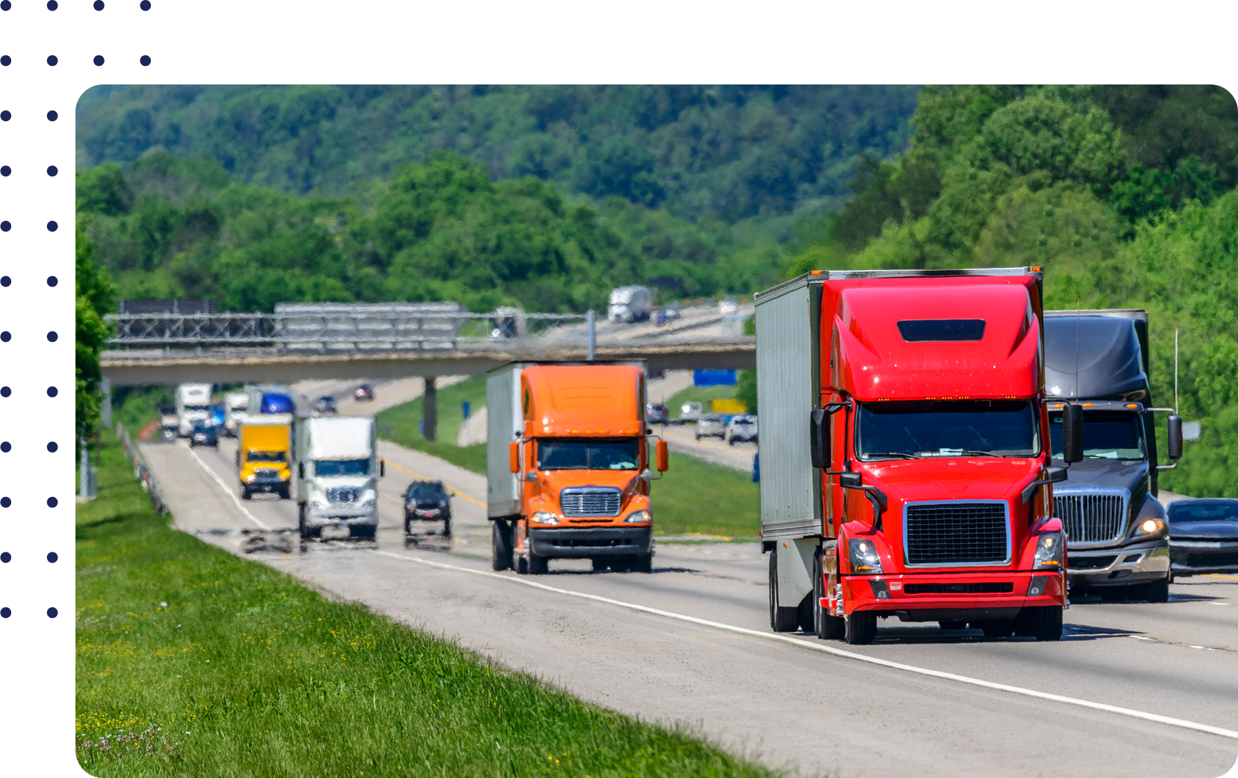 Trucks in various colors drive down a divided highway surrounded by greenery, with an overpass and more vehicles visible in the background.