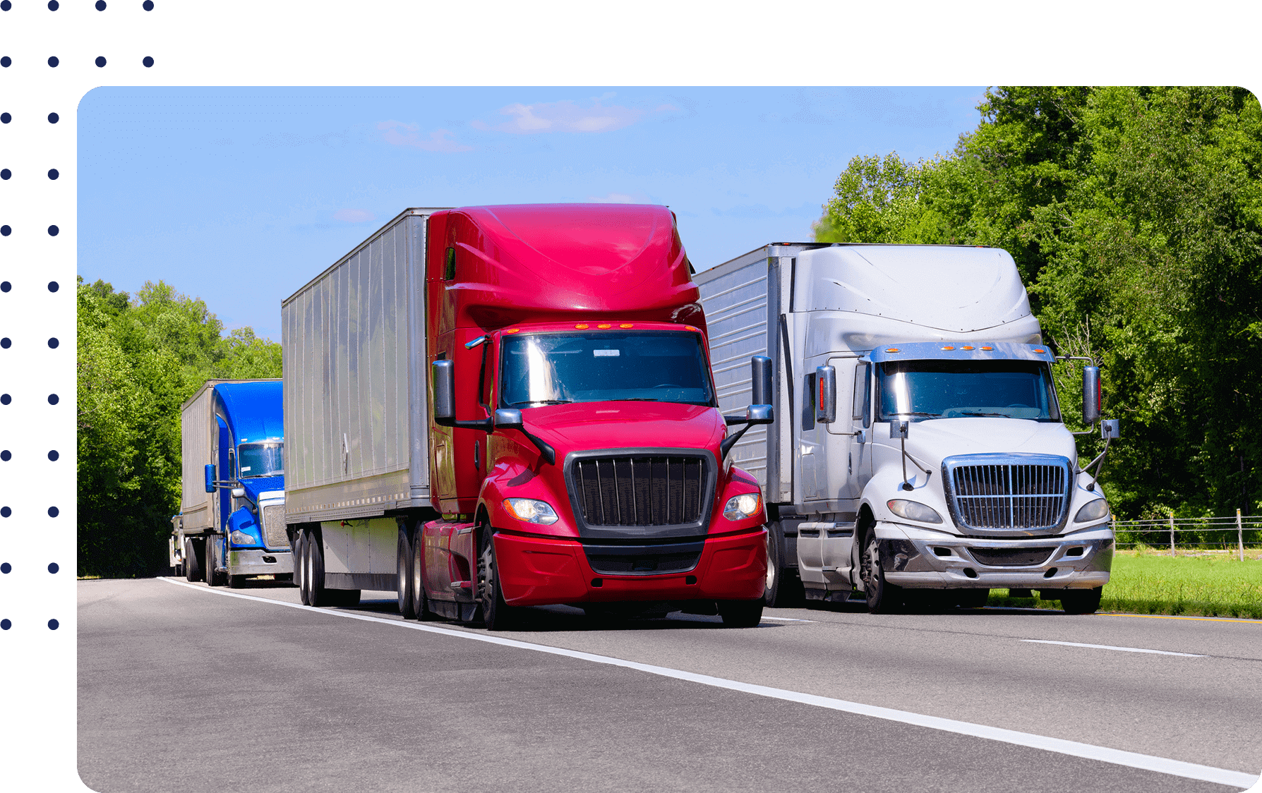 Three semi-trucks, colored blue, red, and silver, drive on a highway surrounded by green trees under a clear blue sky.