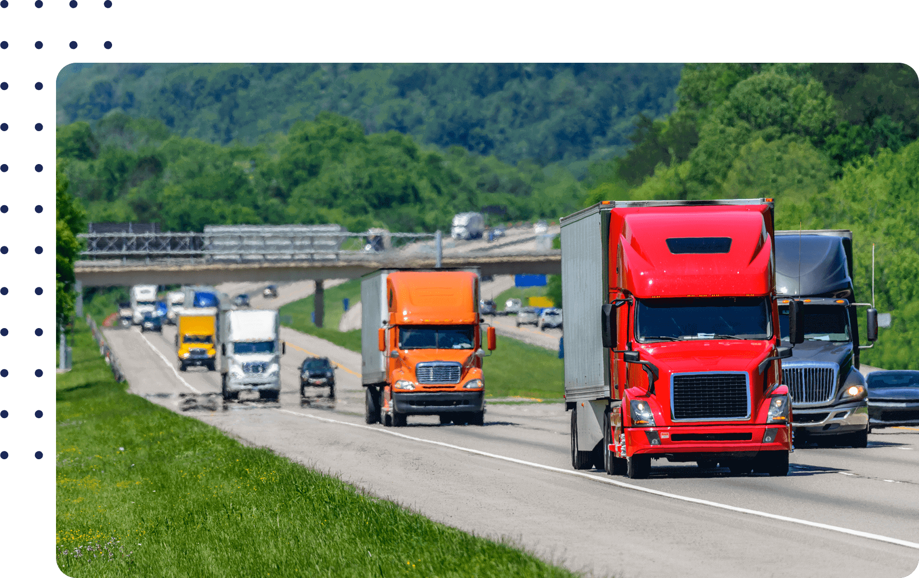 Trucks in various colors drive down a divided highway surrounded by greenery, with an overpass and more vehicles visible in the background.
